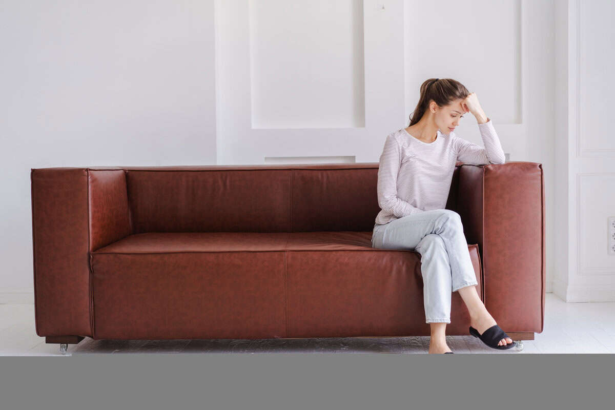 ソファに座りながら悩みごとを考える女性｜40代独身女性に潜む不安や迷いをイメージ