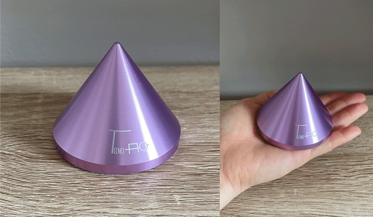 ミニエネルギーバランサー(TAMB01)の本体と、手のひらに乗せたサイズ感の比較写真。直径7cm、高さ5.5cmの円錐型の電磁波対策グッズ。パープルの金属製。