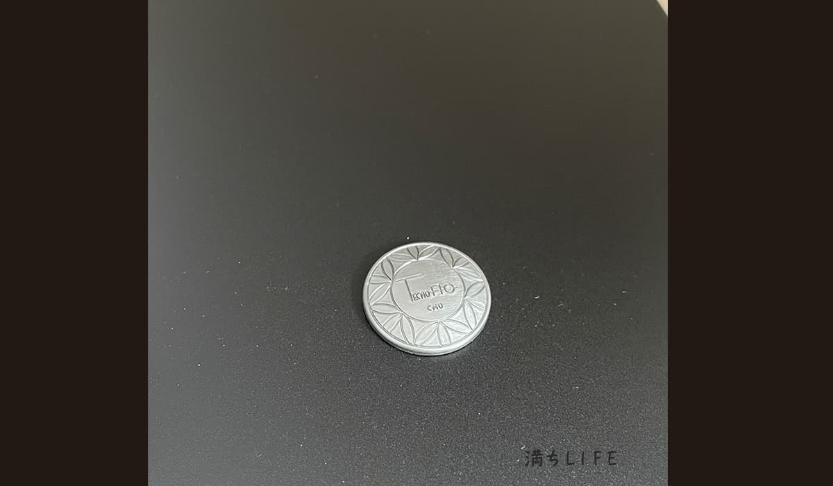 テクノAOの一般家電用PC16（KAPC）、パソコンのハードディスクに貼り付けた状態の写真。直径約2.5cmのシルバーの電磁波対策用チップ。中央にTecnoAOロゴが刻印されている。